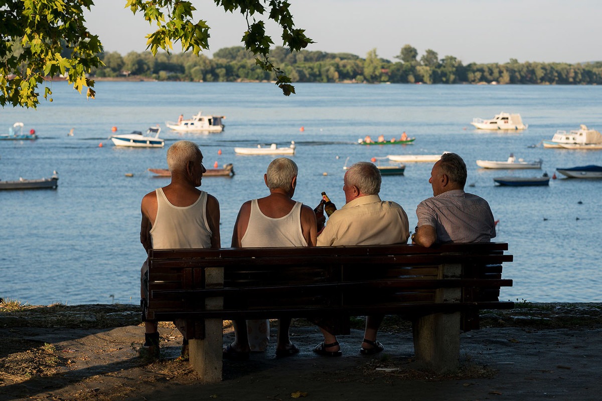 penzioneri sede na klupi na keju pored dunava